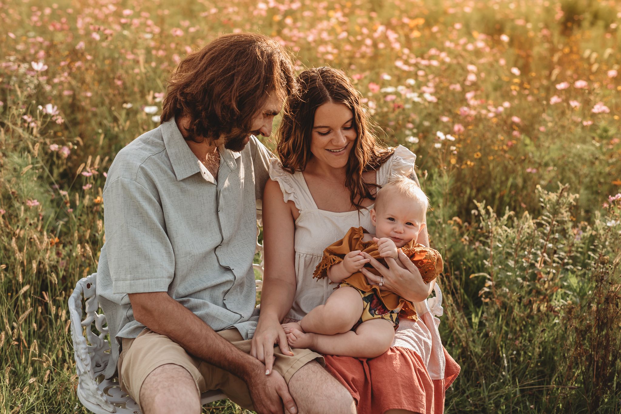 family sitting in a flower field, Mom and Dad admiring their little girl