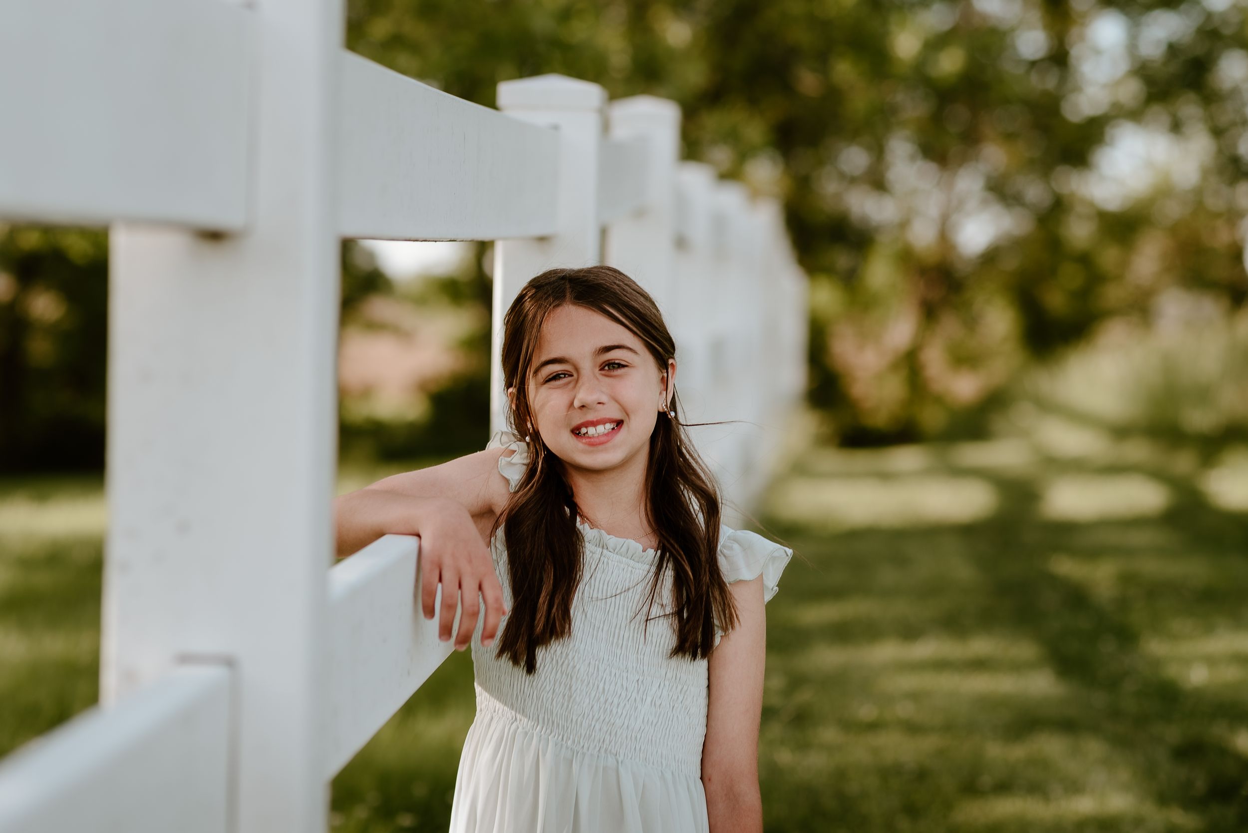 Little girl standing next to white fence
