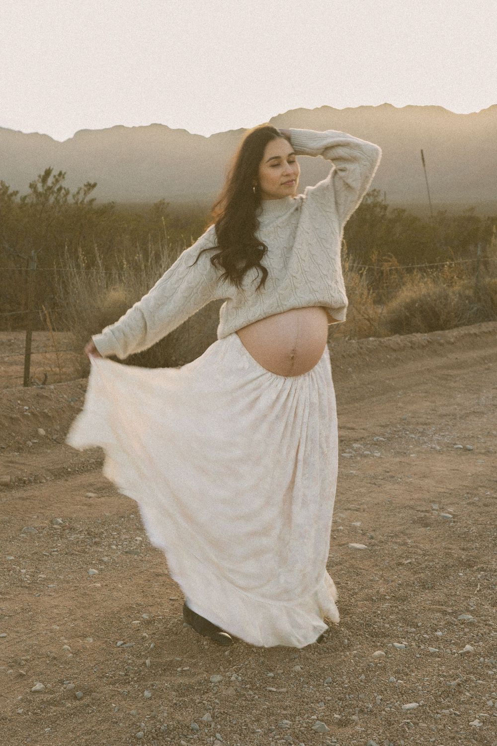 A person in a flowing white dress dances gracefully in a desert landscape at sunset, creating ethereal movement.