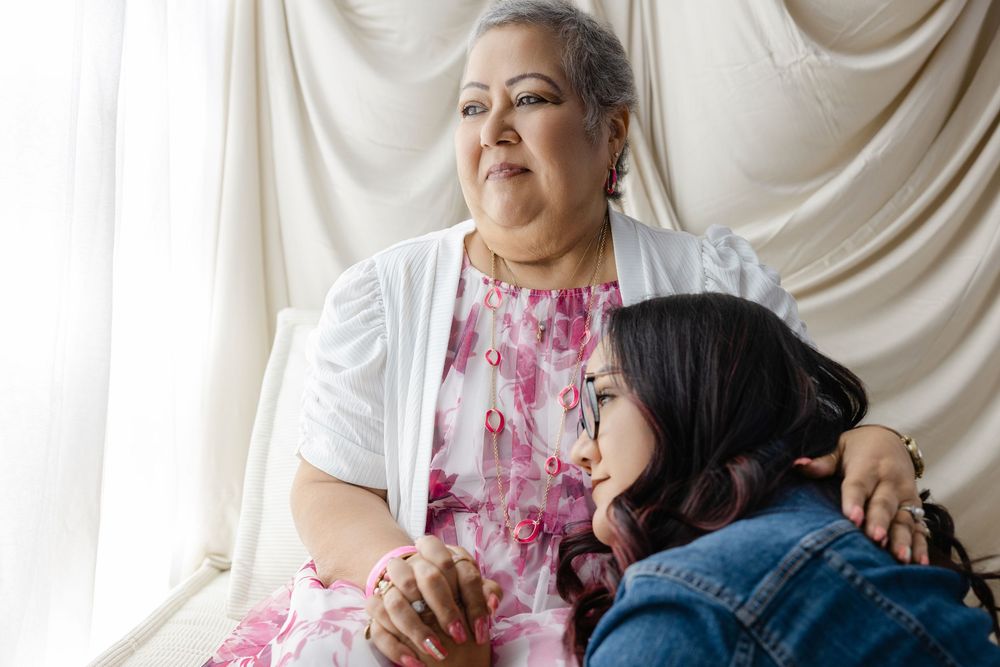 An older woman and young girl sit together by a window, sharing a tender multigenerational moment.
