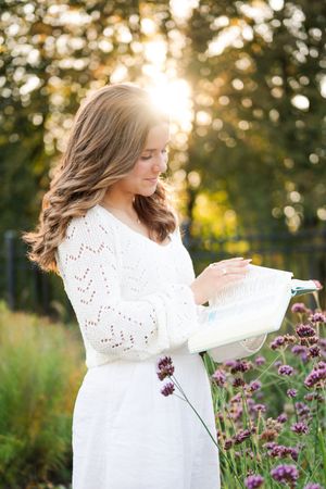 A woman in a white dress stands among purple wildflowers during golden hour in a garden setting.