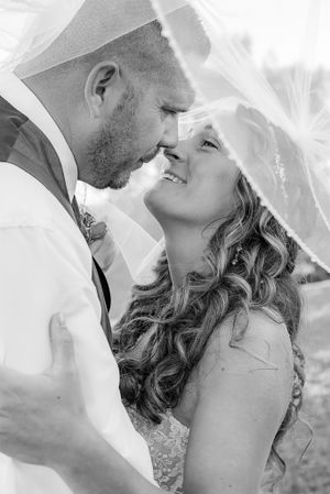 A romantic black and white wedding photo shows a tender moment between newlyweds embracing under a veil.