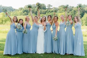 Wedding party poses in light blue bridesmaid gowns and white bridal dress in sunny outdoor garden setting.