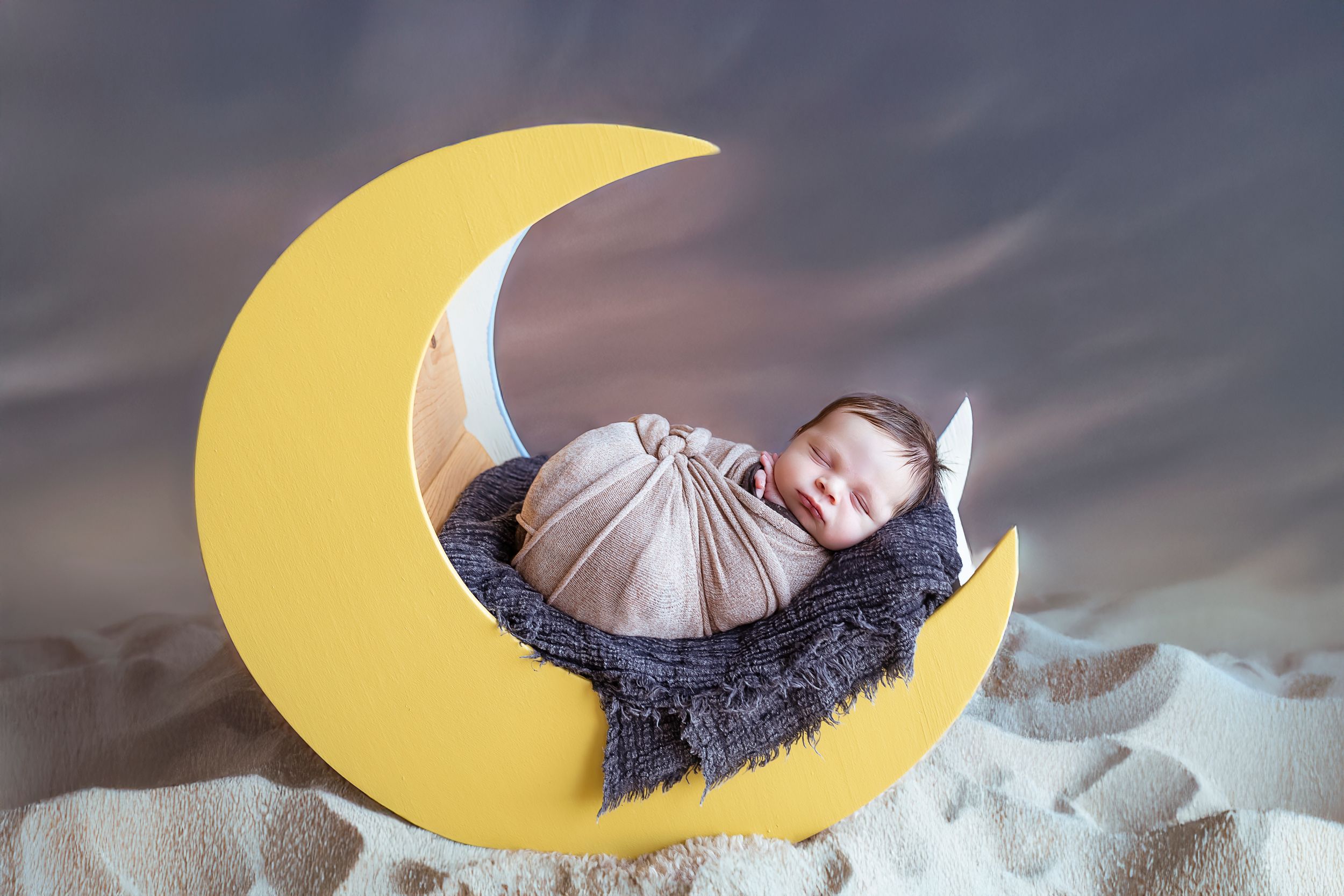 bebe posando encima en una luna amarilla bebe esta envuelto en un pano crema