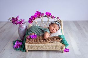 bebe fotografiada con orquideas rosa y bebe ropita verde acostada en cama de rattan