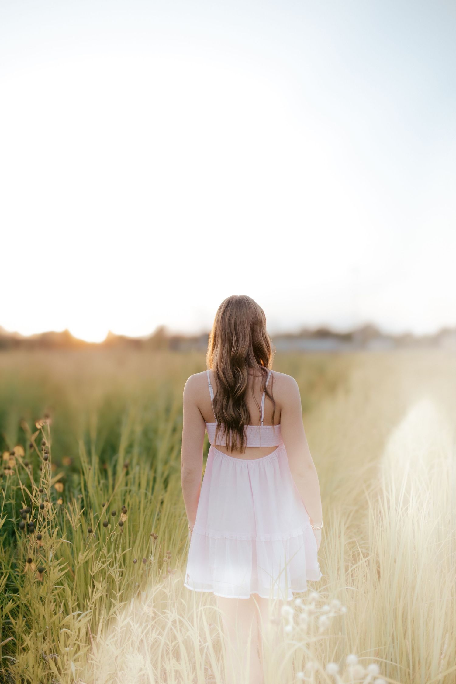 A person in a white dress walks through a golden wheat field at sunset creating a dreamy summer scene.