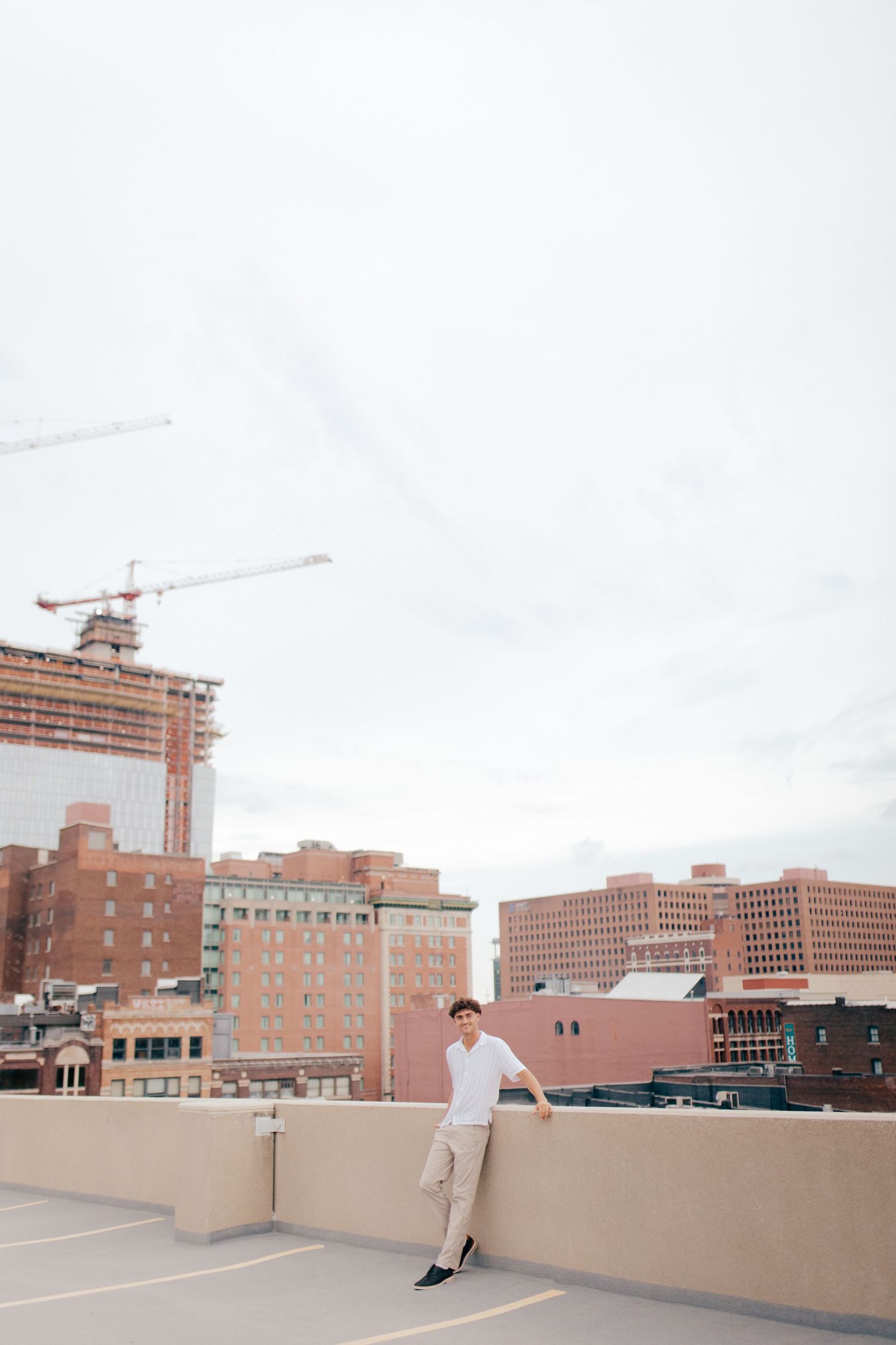 Skateboarder performs tricks on rooftop parking deck with brick buildings and construction cranes in urban backdrop.