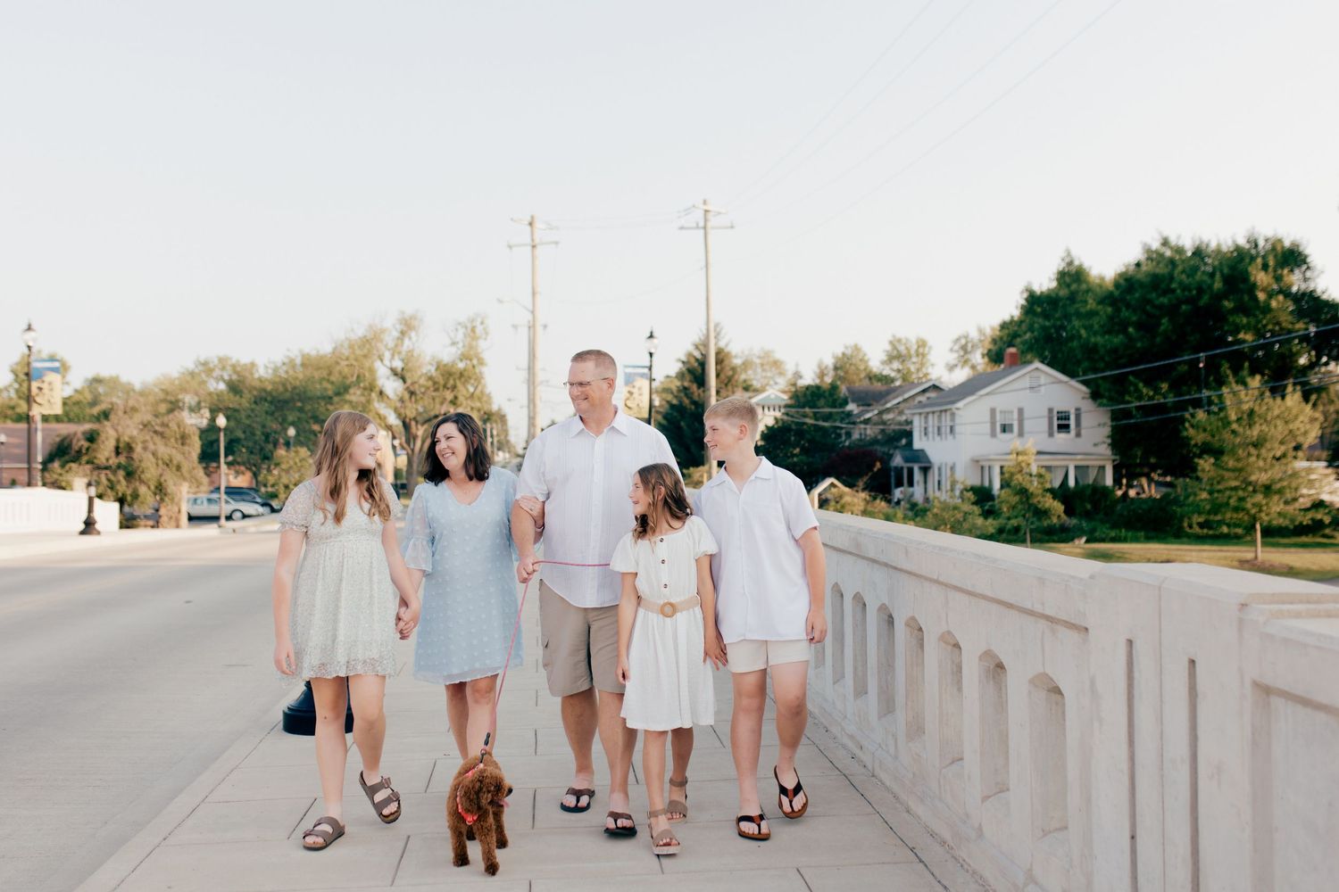 Family wearing white outfits walks together along a beach boardwalk at sunset.