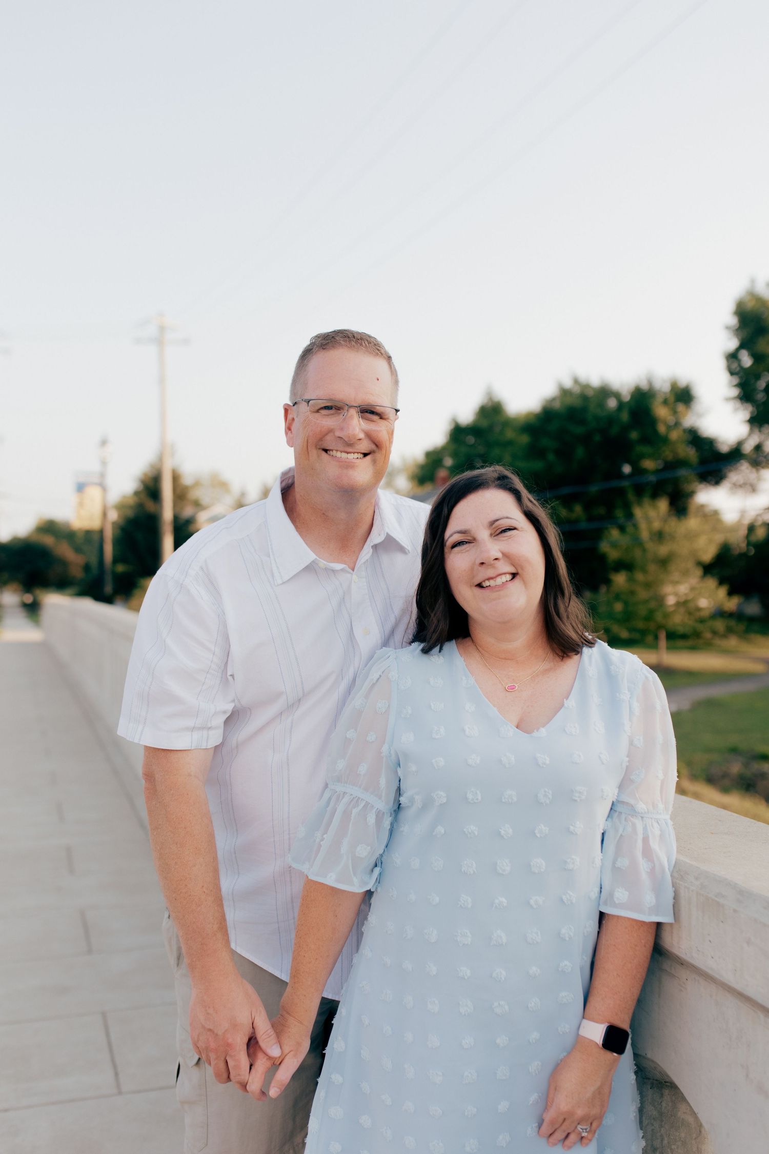 A couple in white and light blue outfits smiling together outdoors during a photo session.