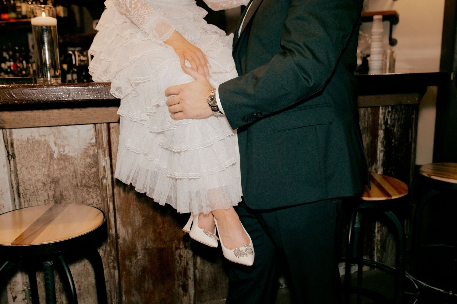 A bride and groom hold hands during their wedding ceremony in a dimly lit, romantic indoor setting.