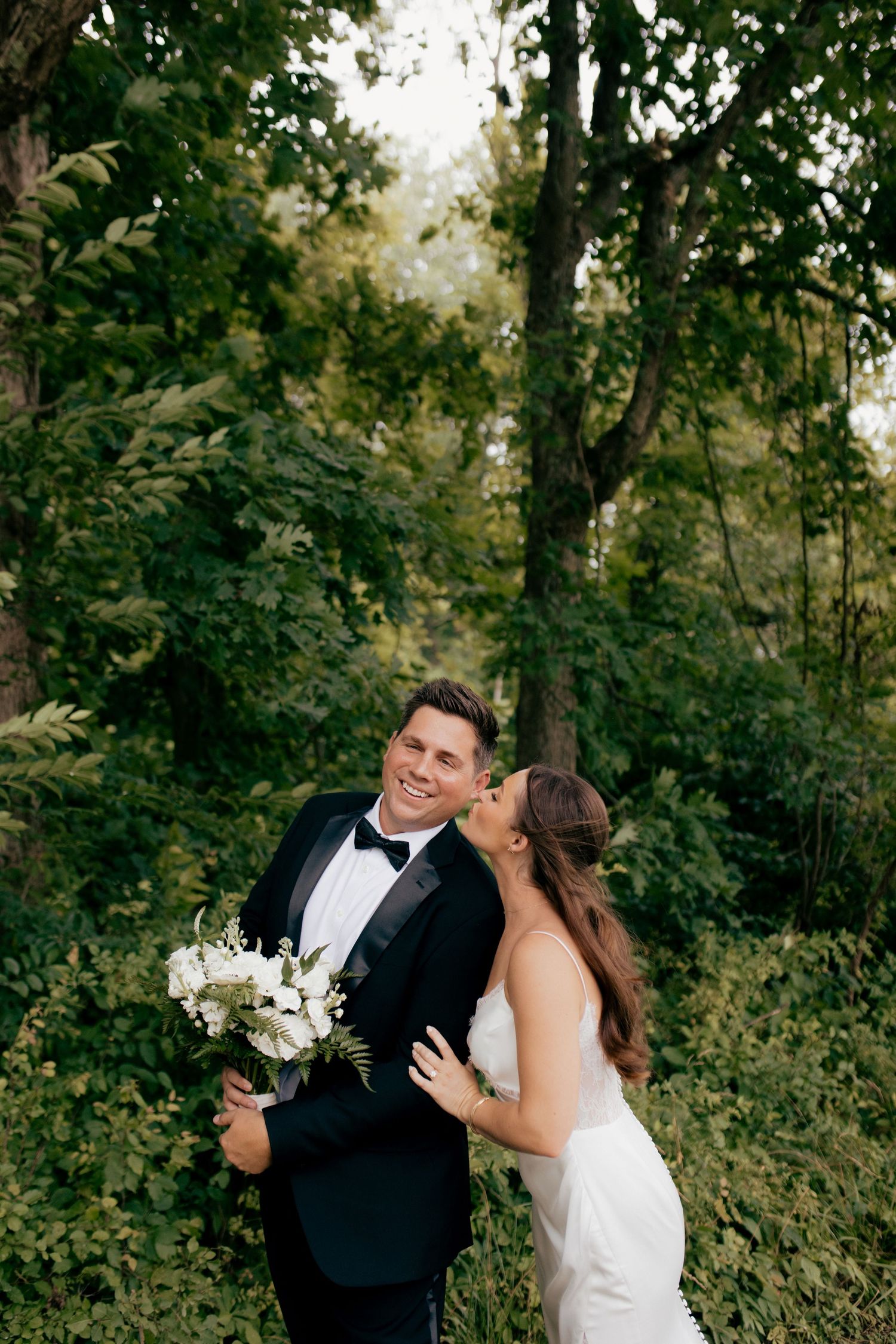 A couple in wedding attire share a joyful moment together in a lush outdoor garden setting.