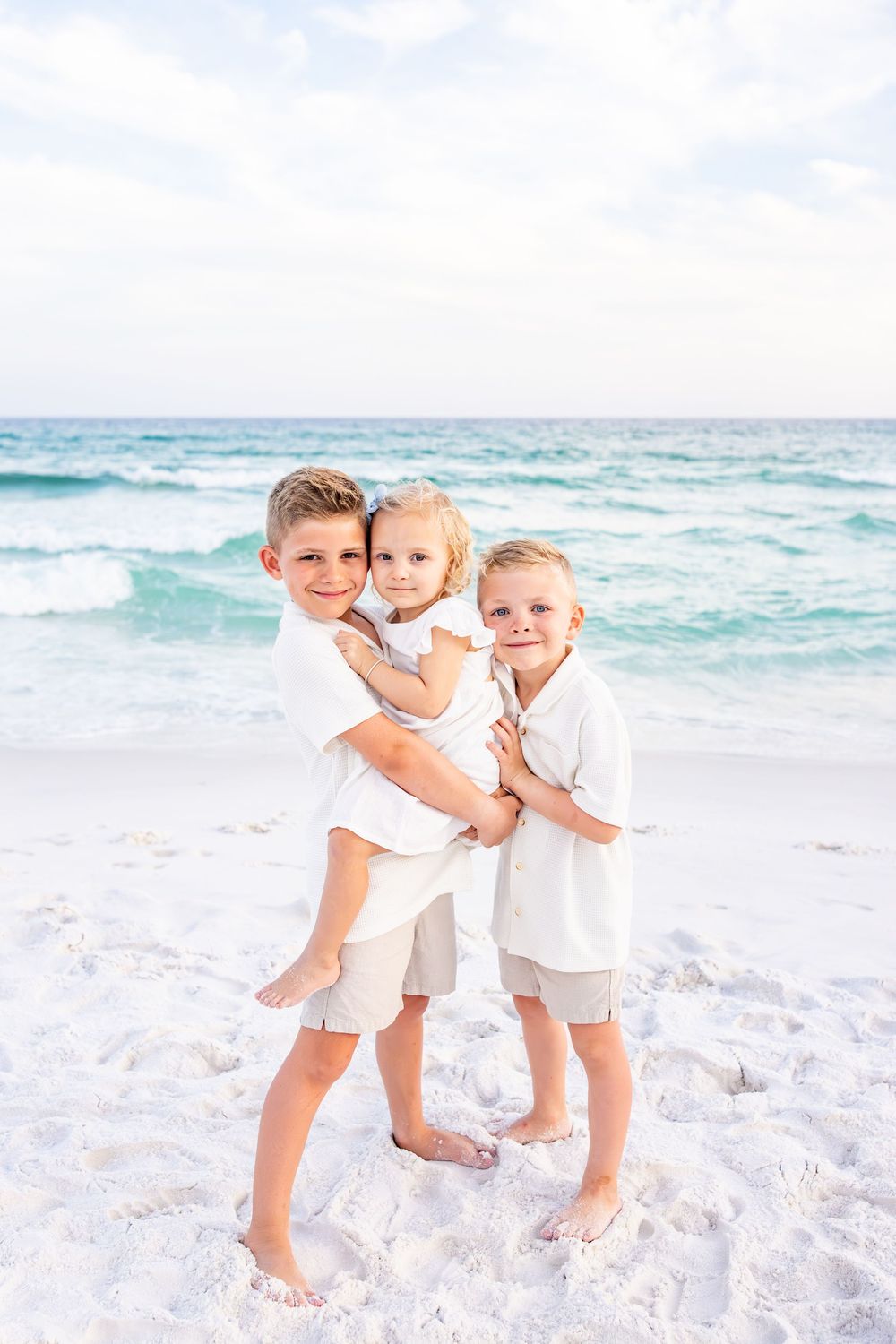Children in white outfits playing together on a pristine white sand beach with turquoise ocean waves in the background.
