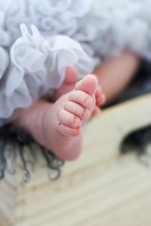 Close up of a baby's tiny foot with ruffled white fabric in soft focus against a light background.