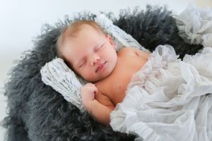Peaceful newborn baby sleeping on soft gray fur blanket wrapped in white delicate fabric.