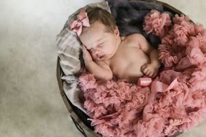 Sleeping infant lying in gray basket surrounded by soft pink tulle fabric.
