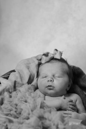 A sleeping newborn baby rests peacefully on soft blankets in a black and white portrait.
