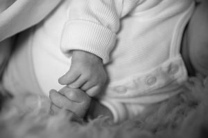Close-up black and white image of a tiny baby's hand resting on soft textured fabric.