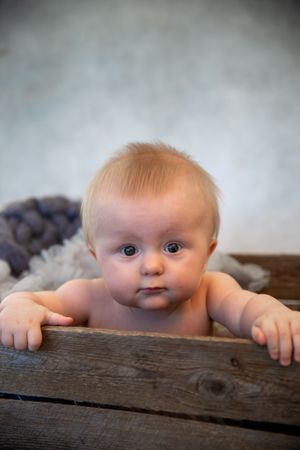 Baby rests arms on rustic wooden surface while looking up with wide curious eyes.