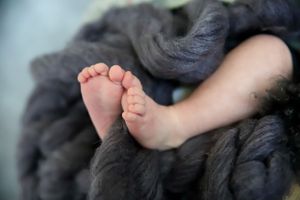 Tiny baby feet rest on soft grey blanket in close up detail shot focusing on delicate toes.