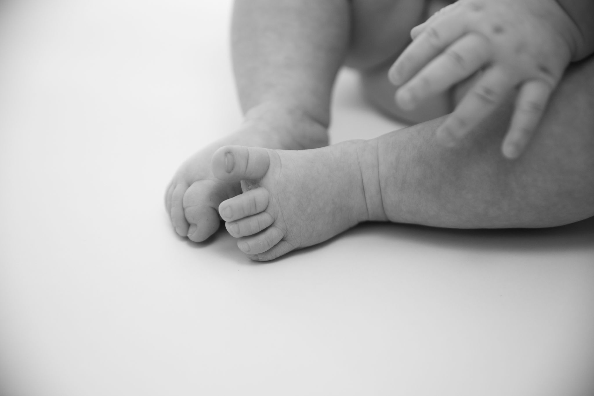 Close-up black and white photo of tiny baby feet and hands against a white background.