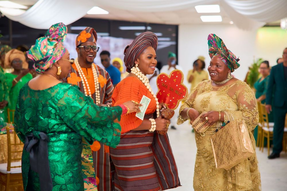 People celebrate at a Nigerian wedding ceremony wearing traditional green and orange attire while dancing and socializing.