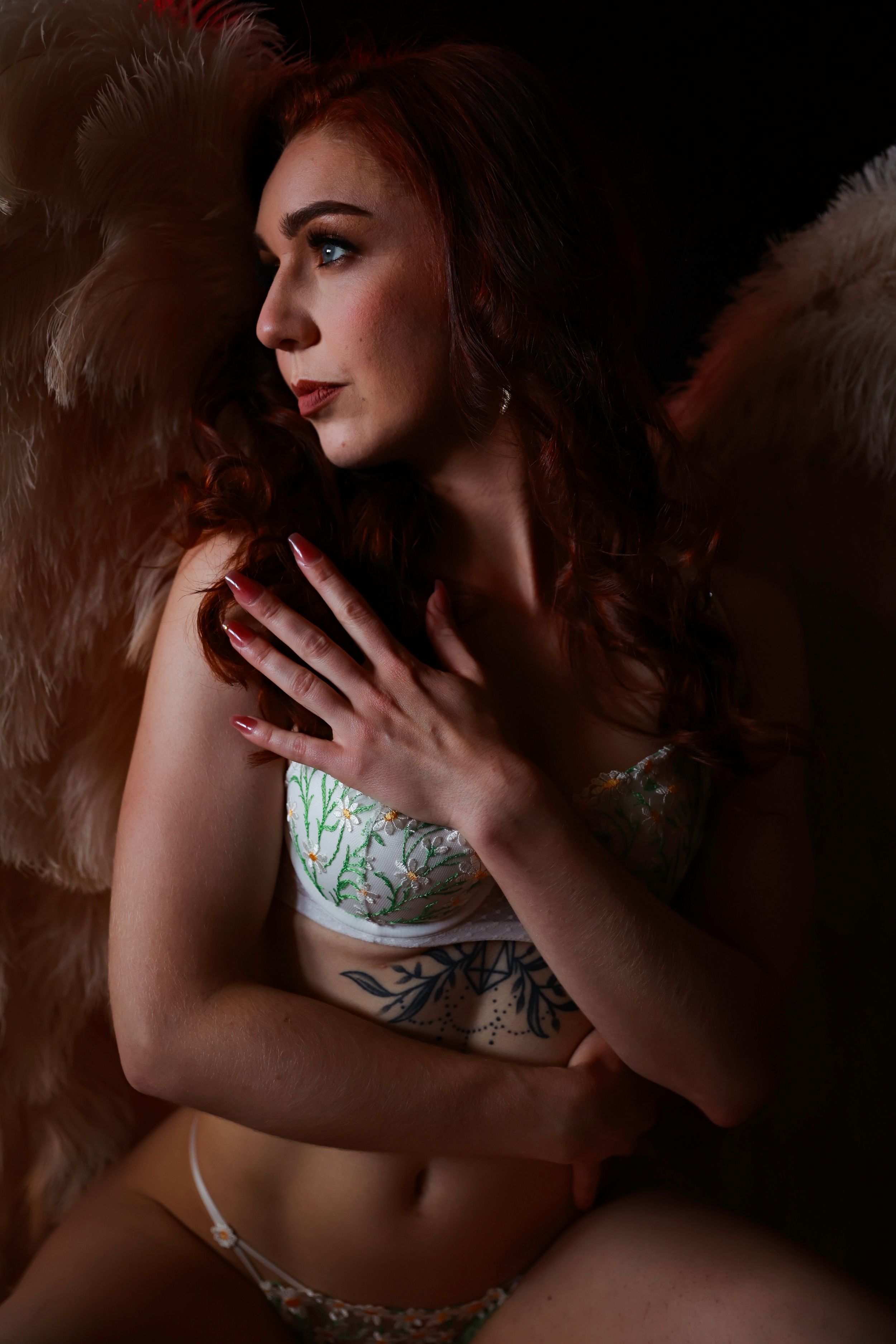 Moody boudoir portrait with dramatic lighting, floral lingerie details, and pink angel wings.