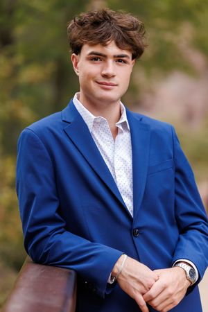 Young man in blue blazer and white dress shirt smiles outdoors in a professional portrait photo.