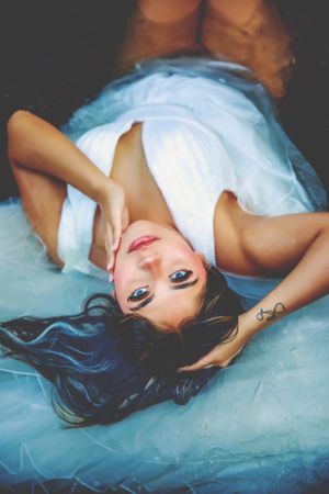 Artistic overhead portrait of model in white dress with dark hair against blue backdrop.