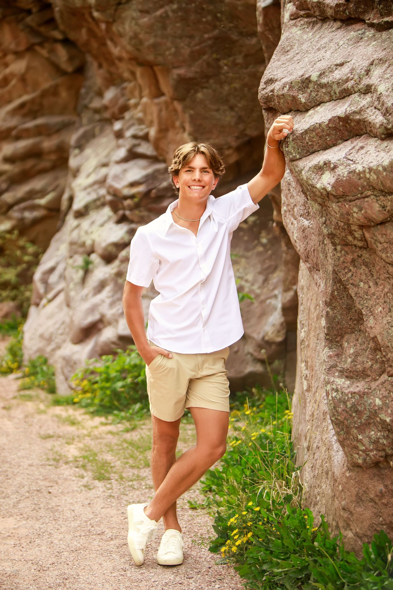 A casual outdoor portrait against rocky cliff wall wearing white shirt and khaki shorts.