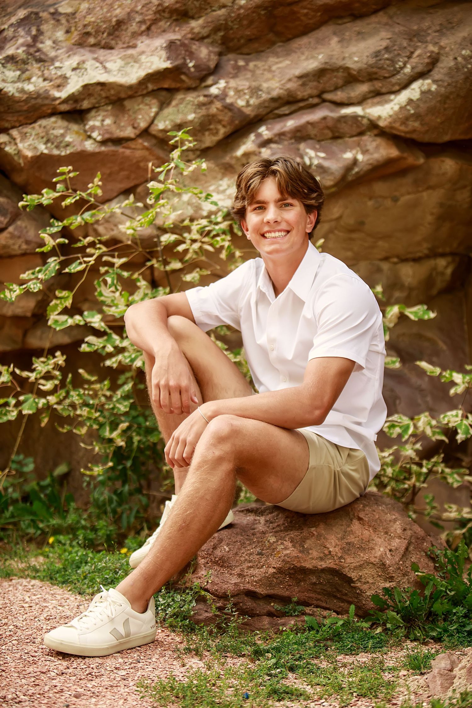 A relaxed outdoor portrait sitting on rock formation in white shirt and khaki shorts.