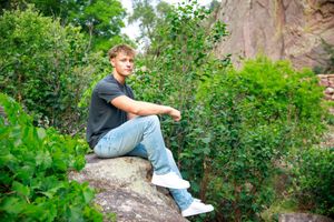 Person sitting on a large boulder in a lush green forest setting while enjoying the natural surroundings.
