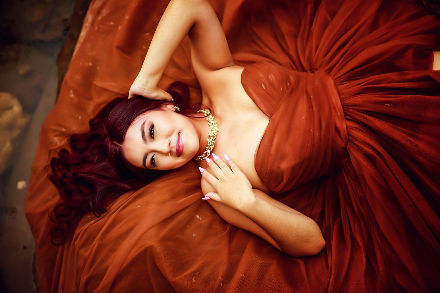 A person in a flowing burgundy red gown poses elegantly against a dark background in a series of artistic portraits.