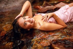 A portrait of a person in pink dress laying on colorful rocks by water.