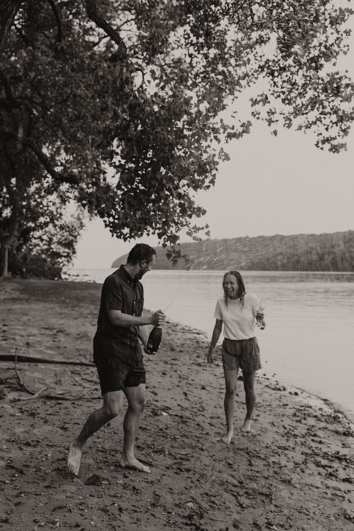 Couple shares playful moments on a riverbank in black and white.