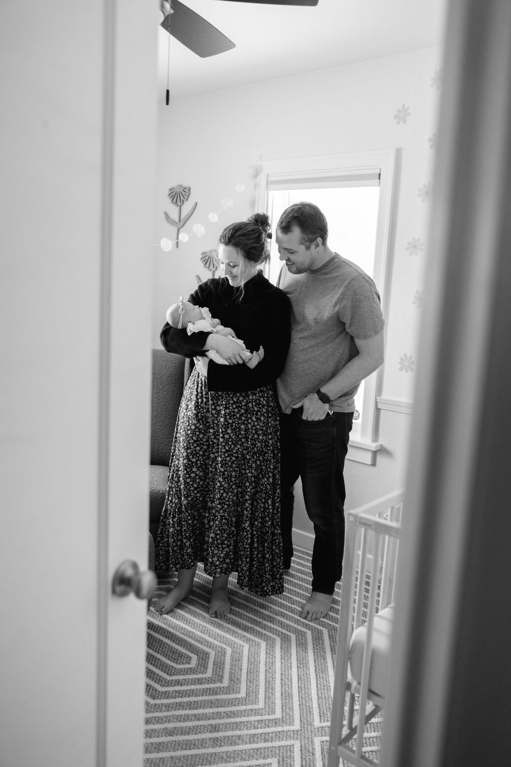 Black and white photo of new parents holding their newborn baby in a decorated nursery room.