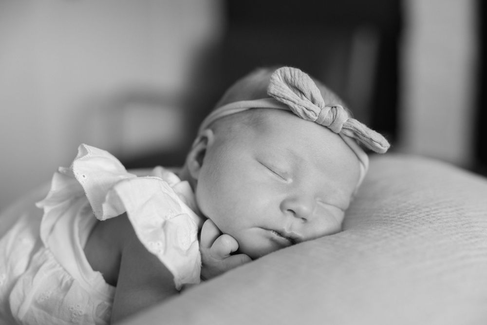 Black and white close-up of a sleeping newborn baby girl wearing a bow headband.