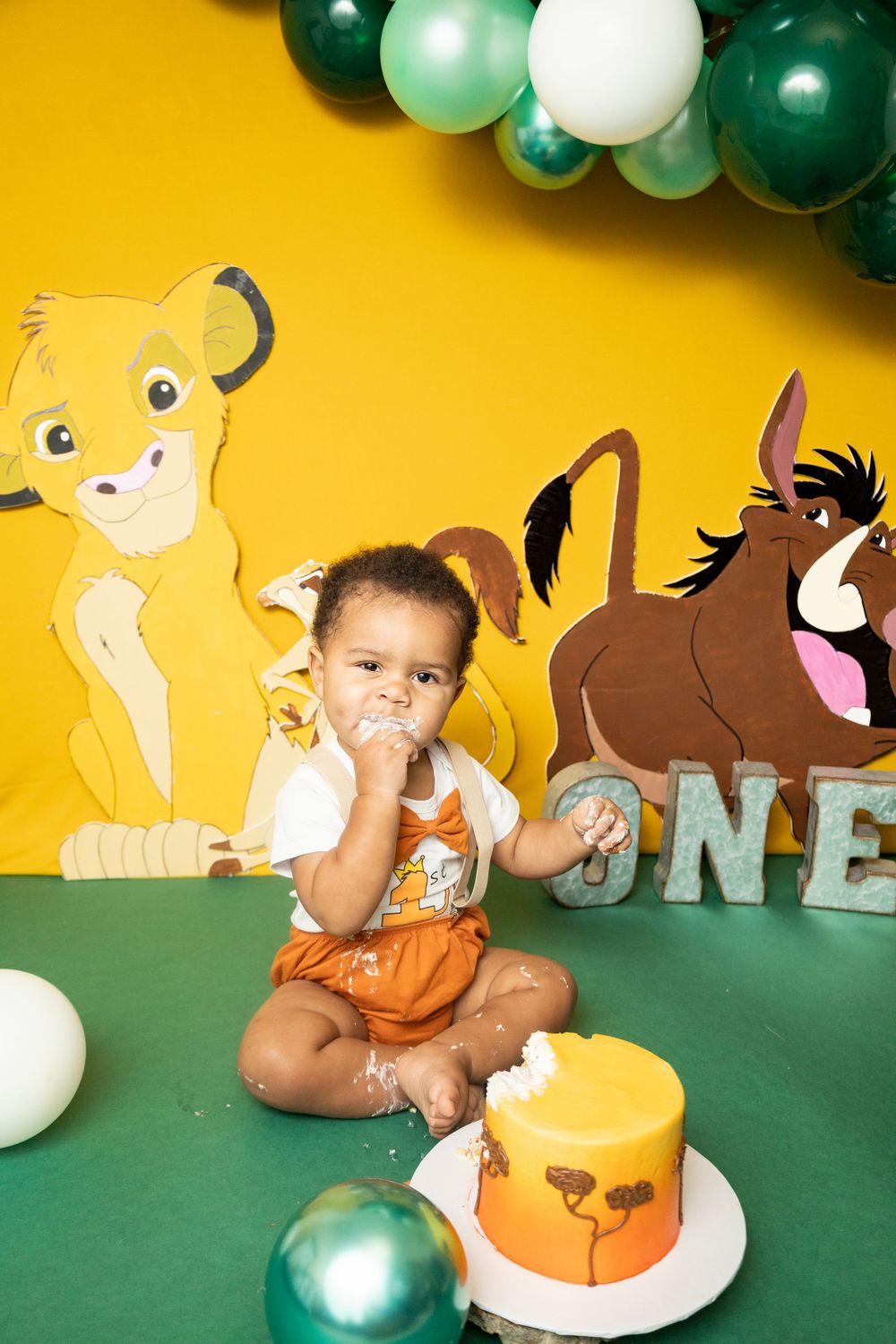 Baby boy eating Lion King birthday cake surrounded by Simba decorations.