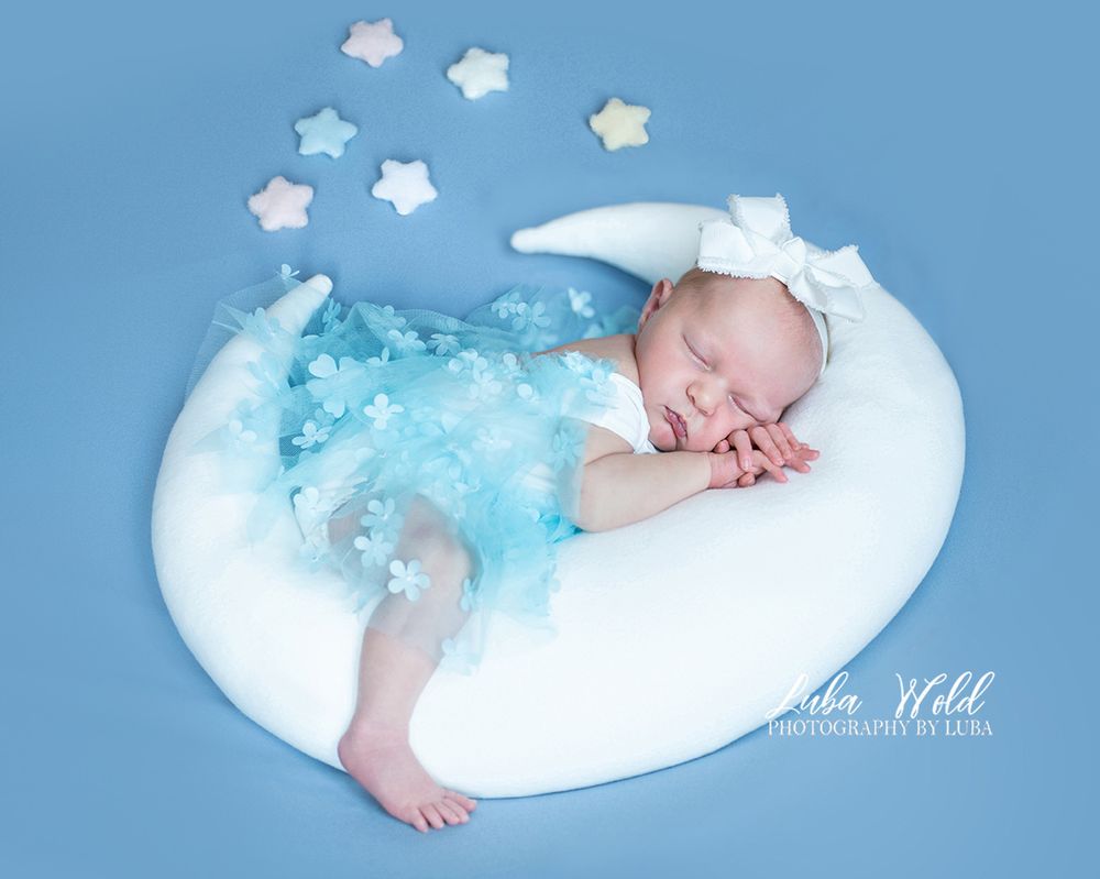 newborn baby girl laying on a white moon prop wearing blue dress by studio photographer in Post Falls Idaho Luba Wold