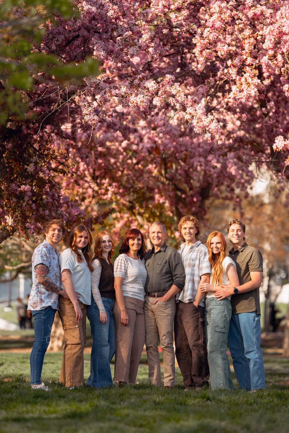 A group stands together on grass beneath blooming pink cherry blossom trees in spring.