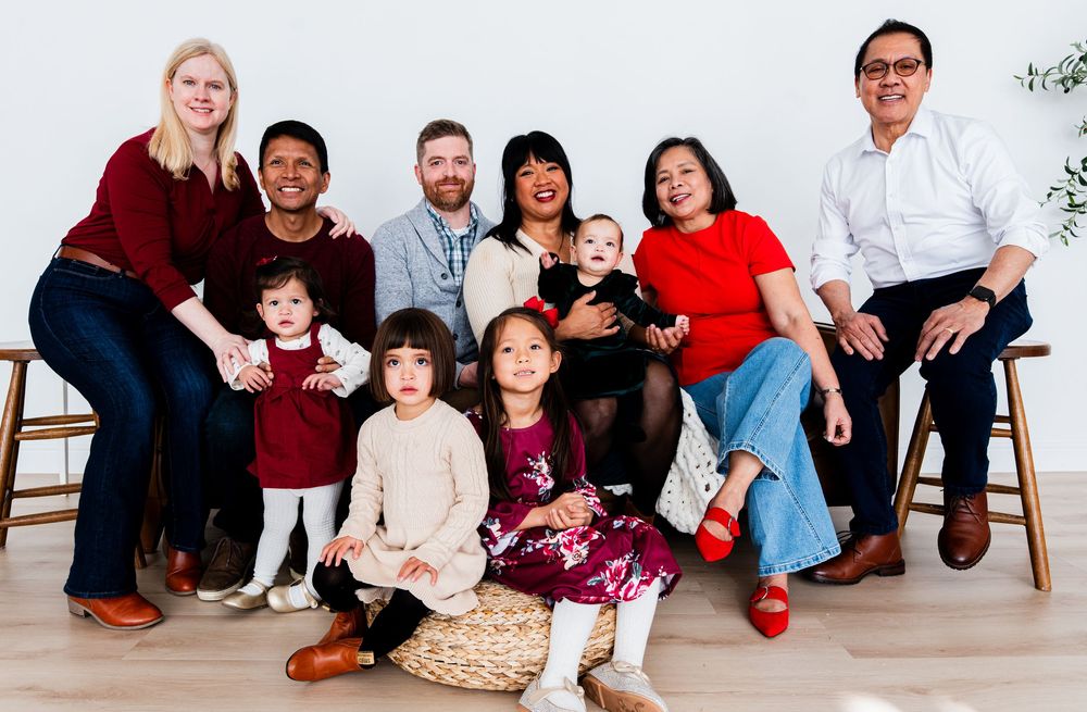 A multi-generational family group sits together for a portrait in a bright studio setting.