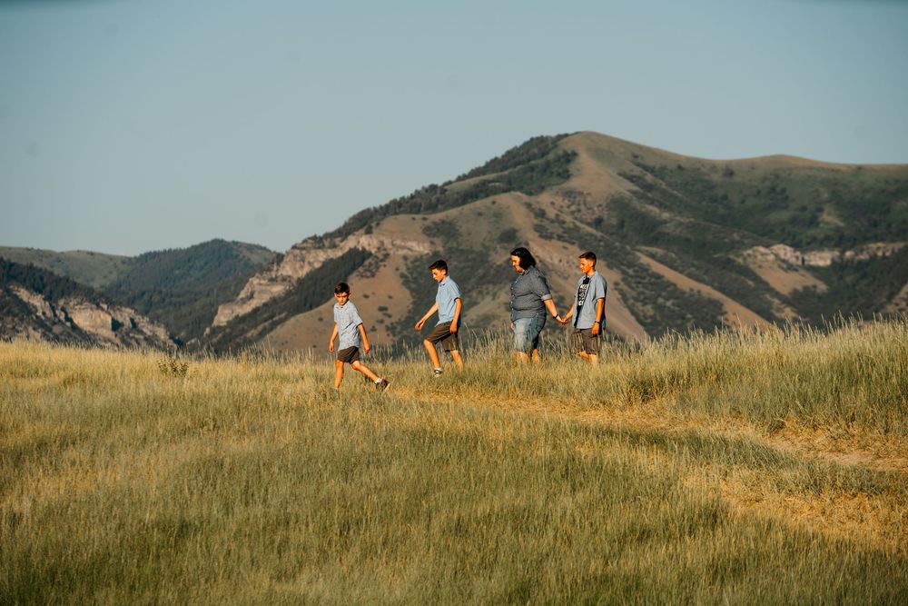 People hiking together through golden grasslands with rolling mountains in the background during sunset.