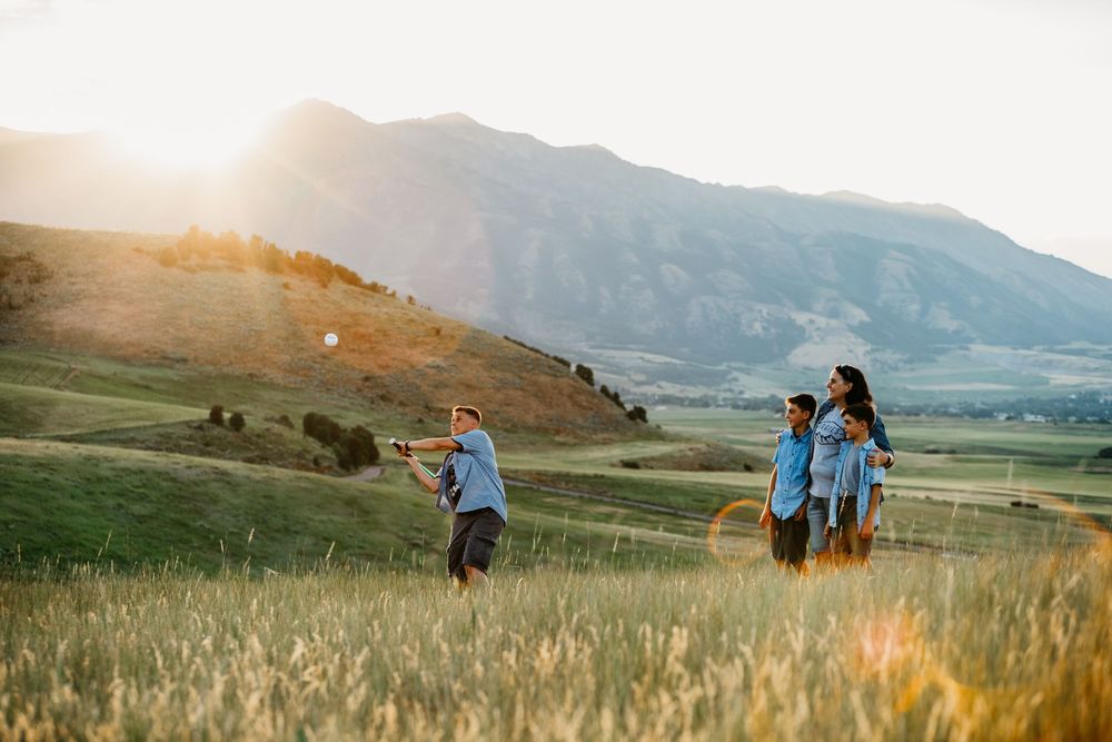 Group of people walking through golden mountain meadows at sunset with rolling hills in background.