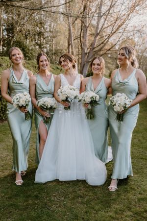 Bridal party in sage green dresses poses with bouquets during an outdoor garden wedding.