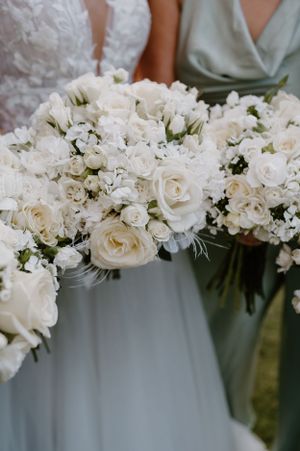 Close-up of elegant white rose and baby's breath wedding bouquets against sage green bridesmaid dresses.