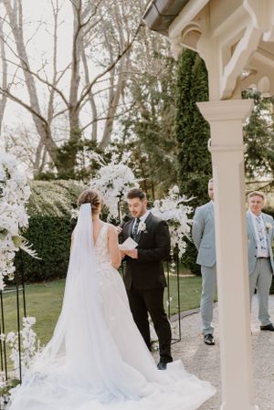 Wedding ceremony taking place under an elegant white archway decorated with flowers.