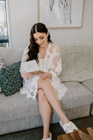 A woman in a delicate white lace robe sits on a gray couch reading a special note or card.Trents Vineyard, Christchurch photographer