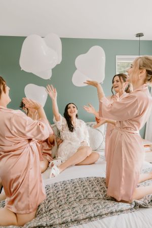 Group in pink satin robes having a playful pillow fight on a bed during pre-wedding celebration.Trents Vineyard, Christchurch photographer