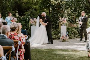 Beautiful outdoor garden wedding ceremony surrounded by lush greenery with guests seated on wooden chairs.