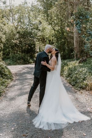 A romantic wedding couple embracing on a sunlit forest path, surrounded by lush greenery and dappled sunlight.