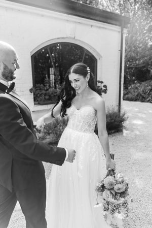 Black and white photo of newlyweds sharing a tender moment outdoors, bride in strapless lace gown holding floral bouquet.